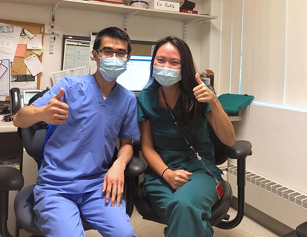 Two seated students in scrubs, giving the thumbs up sign at their externship at the Martha Eliot Center