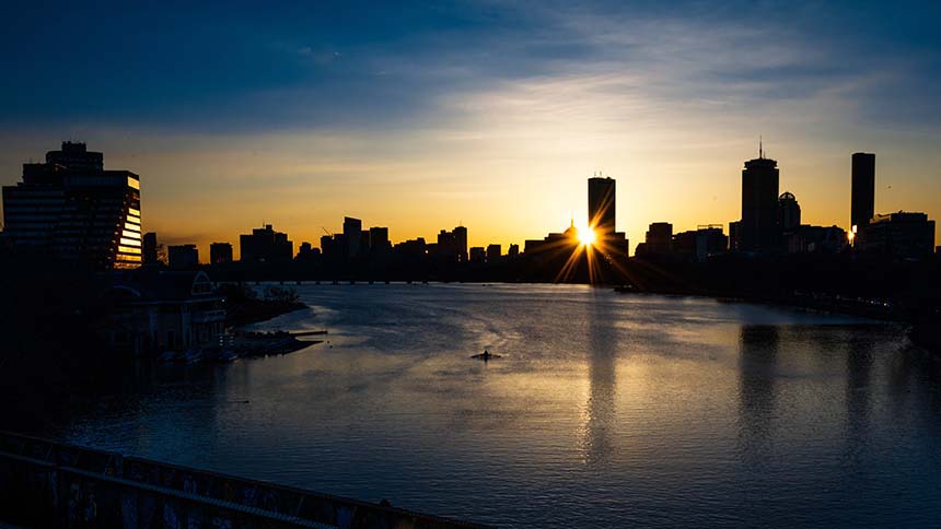 Sunrise over the Charles River with rower on river in front of the Boston skyline