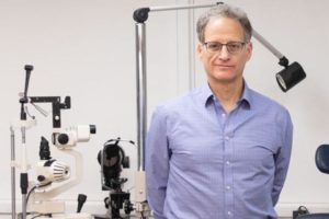 Dr. Barry Kran in blue collar shirt in front of exam area.