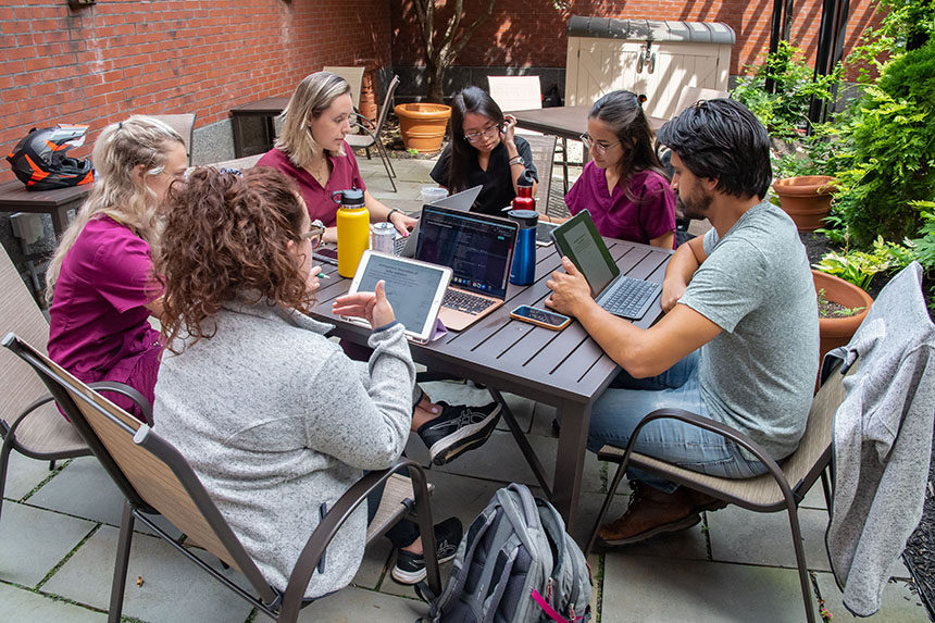 Six students studying together outside in courtyard with laptops open on tabletop