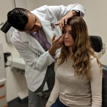 student in white coat doing contact lens assessment on student