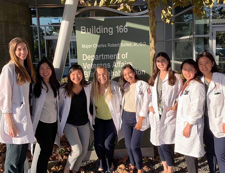 group of 8 female students in white coats in front of building sign