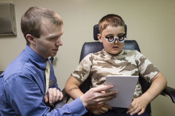 Student helps a young patient in the clinic by holding a reading sample in front of him