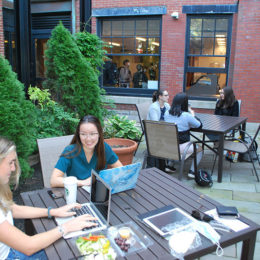 Two groups of students talking and studying in outdoor courtyard at Beacon Street location in the summer