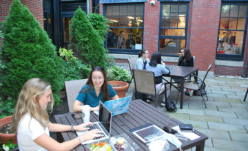 Two groups of students talking and studying in outdoor courtyard at Beacon Street location in the summer