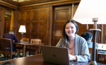 Female student wearing grey sweater smiling while at computer in library