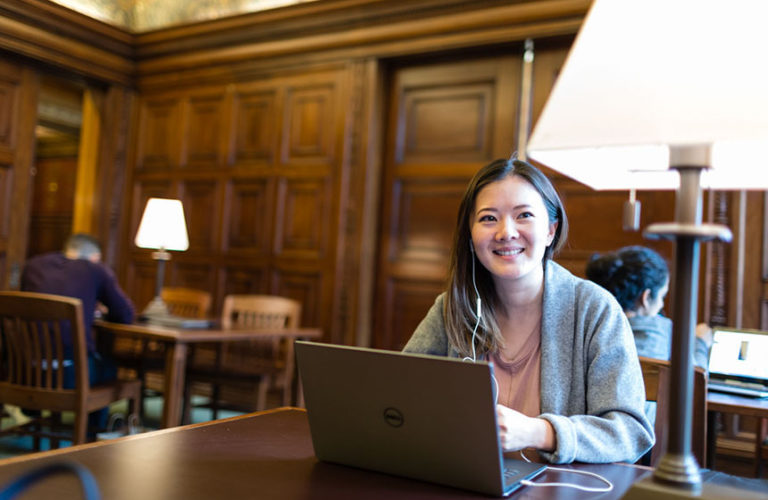 Female student wearing grey sweater smiling while at computer in library