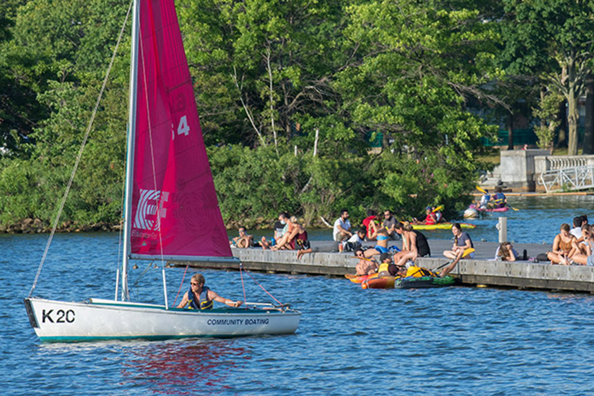 man sailing on the charles river with a group of people on dock behind him