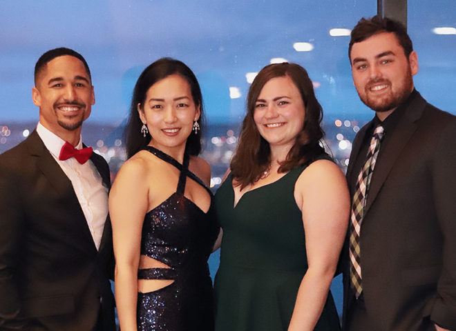 group of students pose in formal wear at event overlooking a city skyline