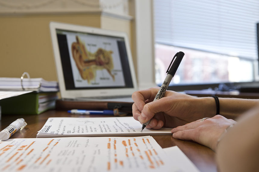 student's hands taking notes while screen with diagram is in background