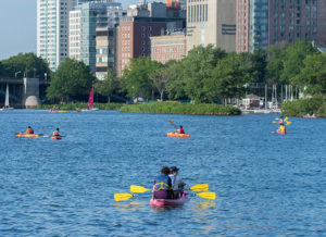 Kayakers on the Charles River with the city skyline in the background.