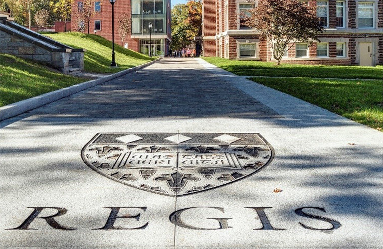 Regis College seal engraved on sidewalk with campus in the background