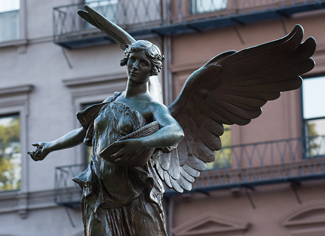 bronze statue of angel with wings and arm outstretched