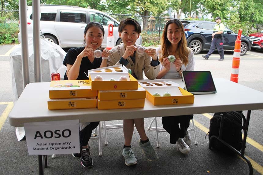 three students holding colorful treats and sitting at white table