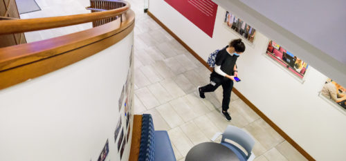 student in scrubs walks past staircase and wall of framed pictures