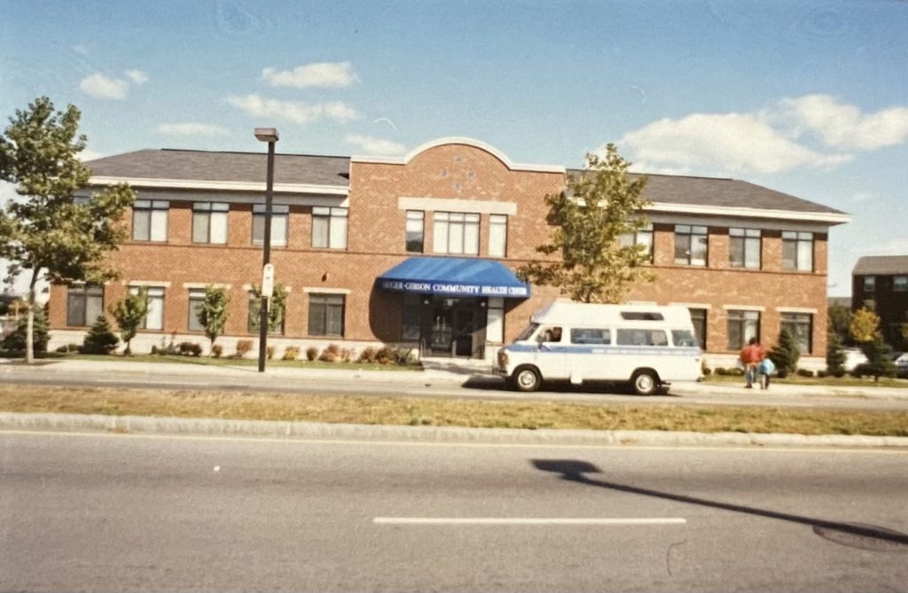old photograph of building exterior with hospital van parked out front