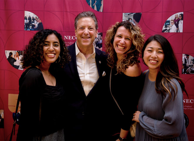 Four people standing in front of red backdrop smiling