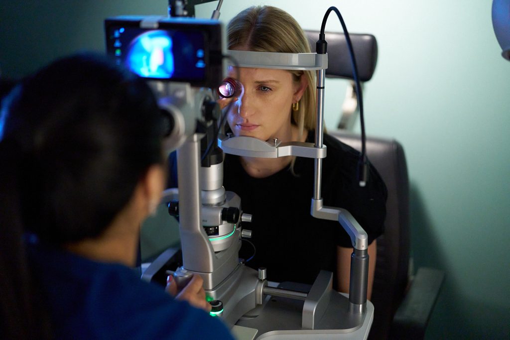 woman with face in optometric equipment while doctor looks at her eye