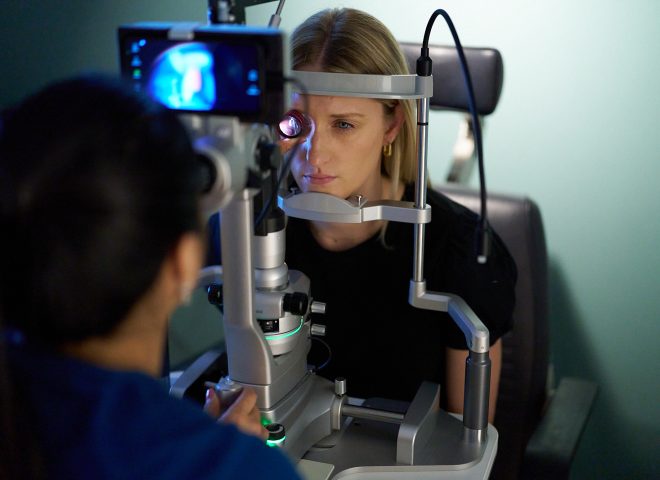 woman with face in optometric equipment while doctor looks at her eye