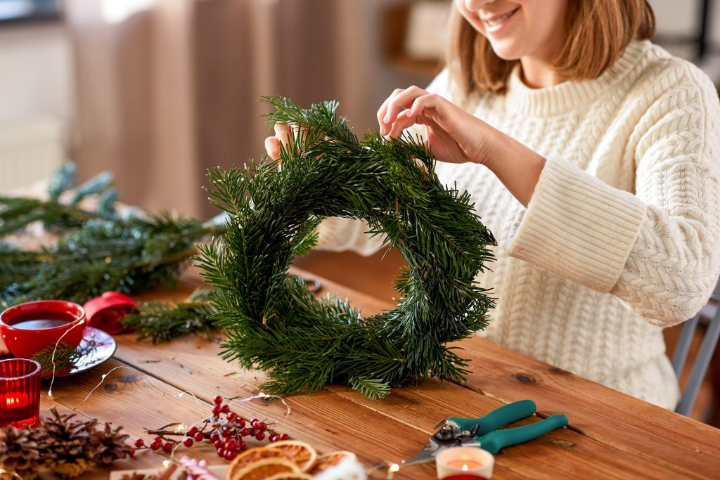close up of happy smiling woman with fir branches making christmas wreath at home