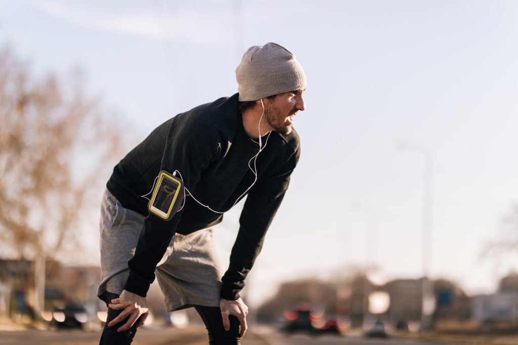 Exhausted male runner resting while left out of breath after jogging in the city.